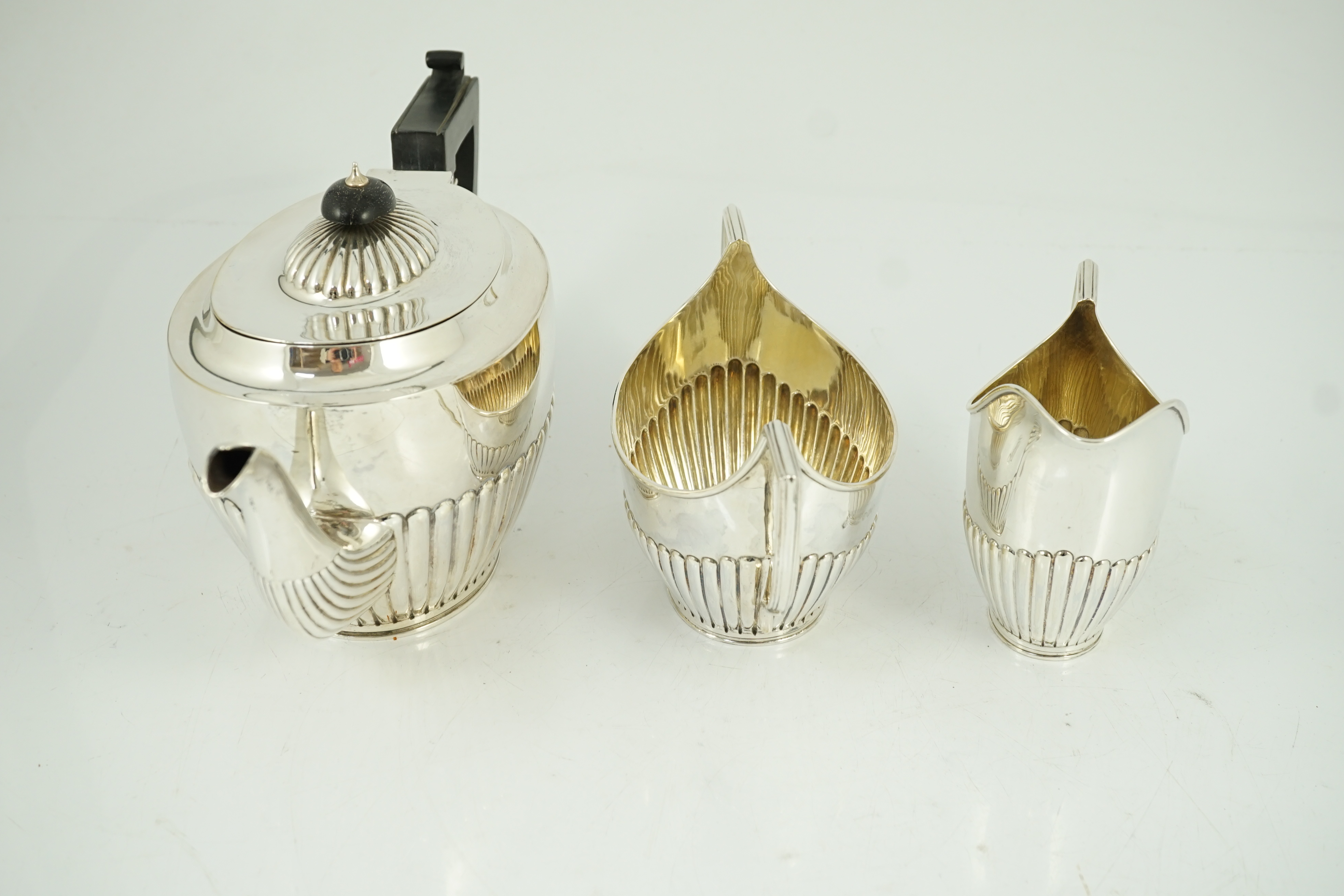 A late Victorian oak cased demi-fluted oval silver three piece tea set, by Martin, Hall & Co